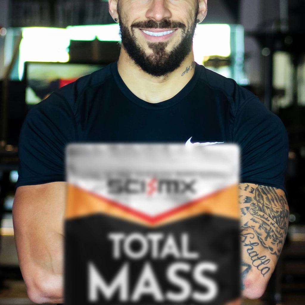Muscular man standing in front of a package of Sci-Mx Total Mass supplement 