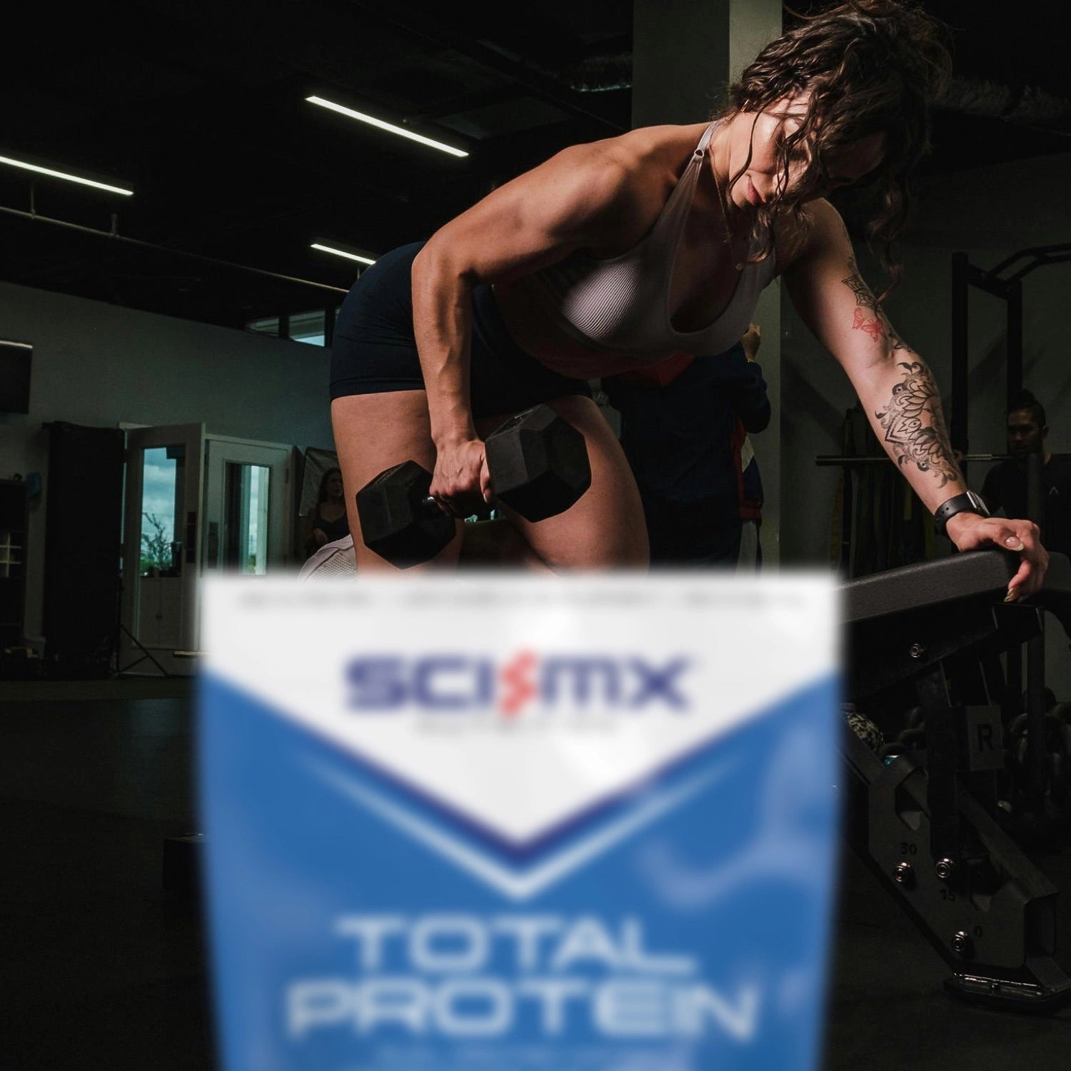 Person lifting weights with a Sci-Mx Total Protein pack in the foreground