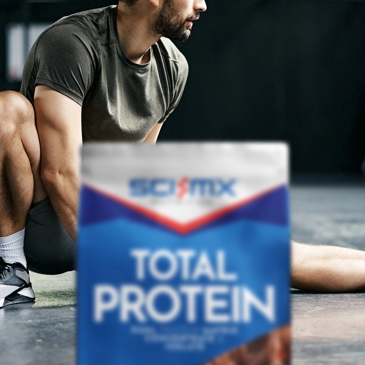 Person stretching on a gym floor with a Sci-Mx Total Protein container in the foreground