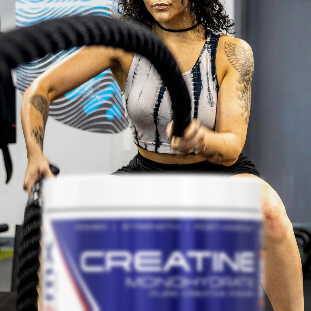 Woman exercising with battle ropes, with a creatine monohydrate container in the foreground.