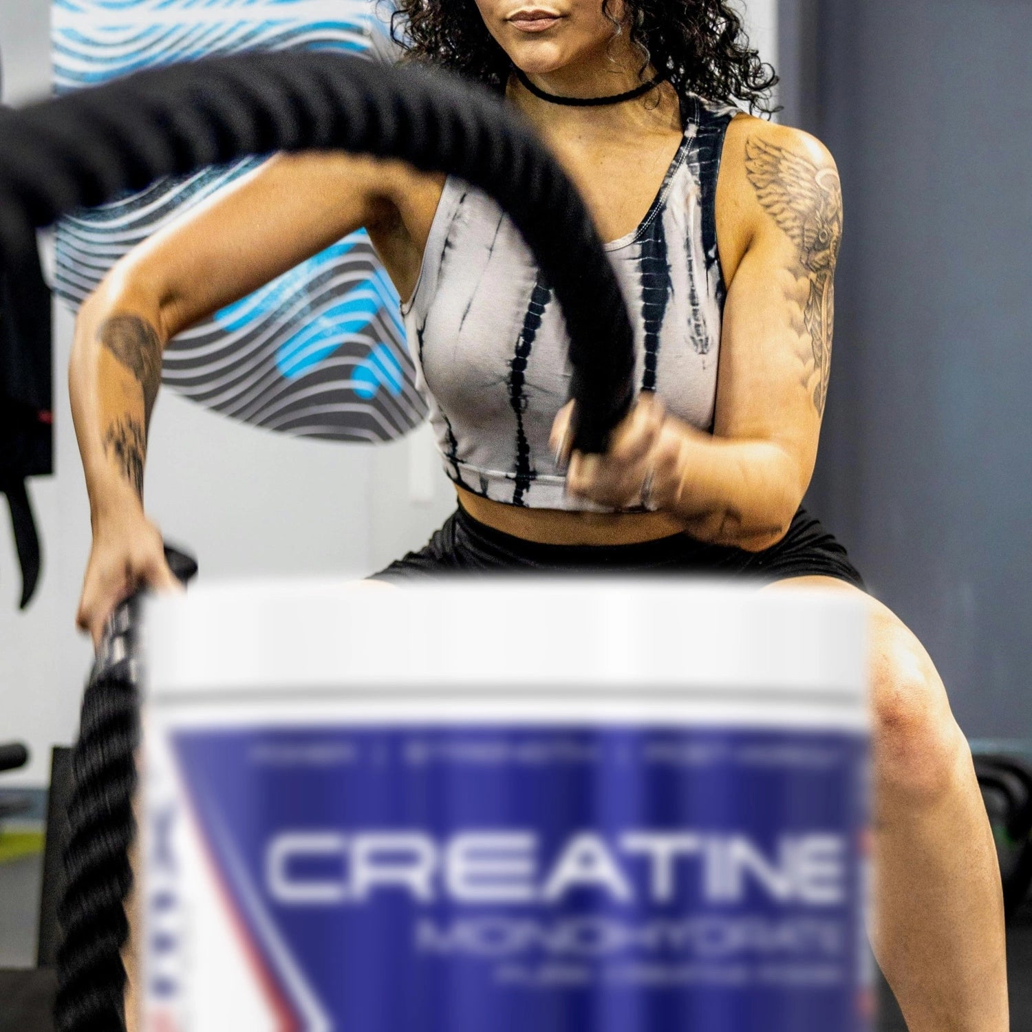 Woman exercising with battle ropes, with a creatine monohydrate container in the foreground.
