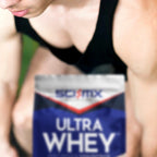 A close-up shot of a person training in a black tank top behind a bag of SCI-MX Ultra Whey protein powder, with the brand and product name clearly visible on the packaging.