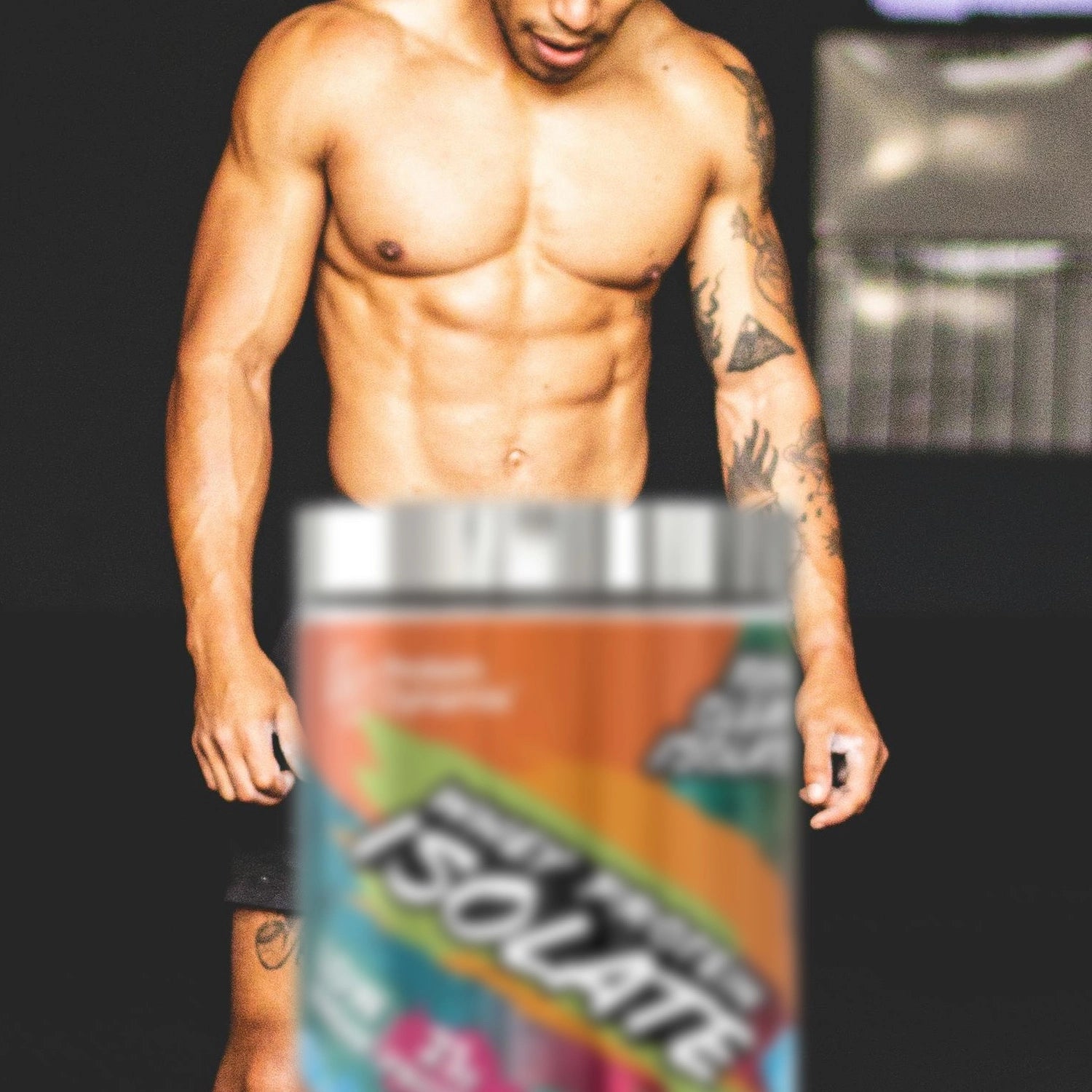 Man with muscular build in gym with a container of Whey Protein Isolate against a dark background