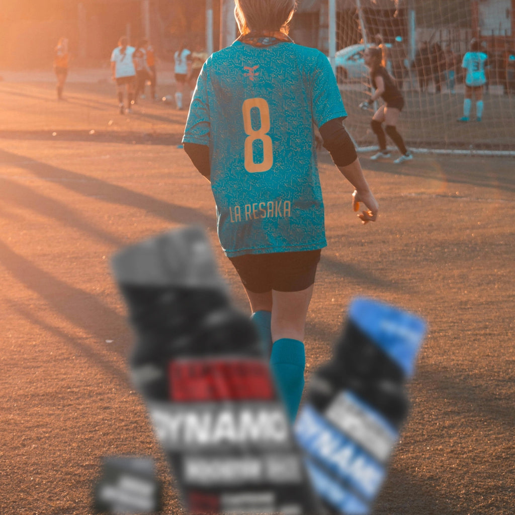 Soccer player in a blue jersey with number 8 on a soccer field during sunset with Protein Dynamix Dynamo Shot in the foreground