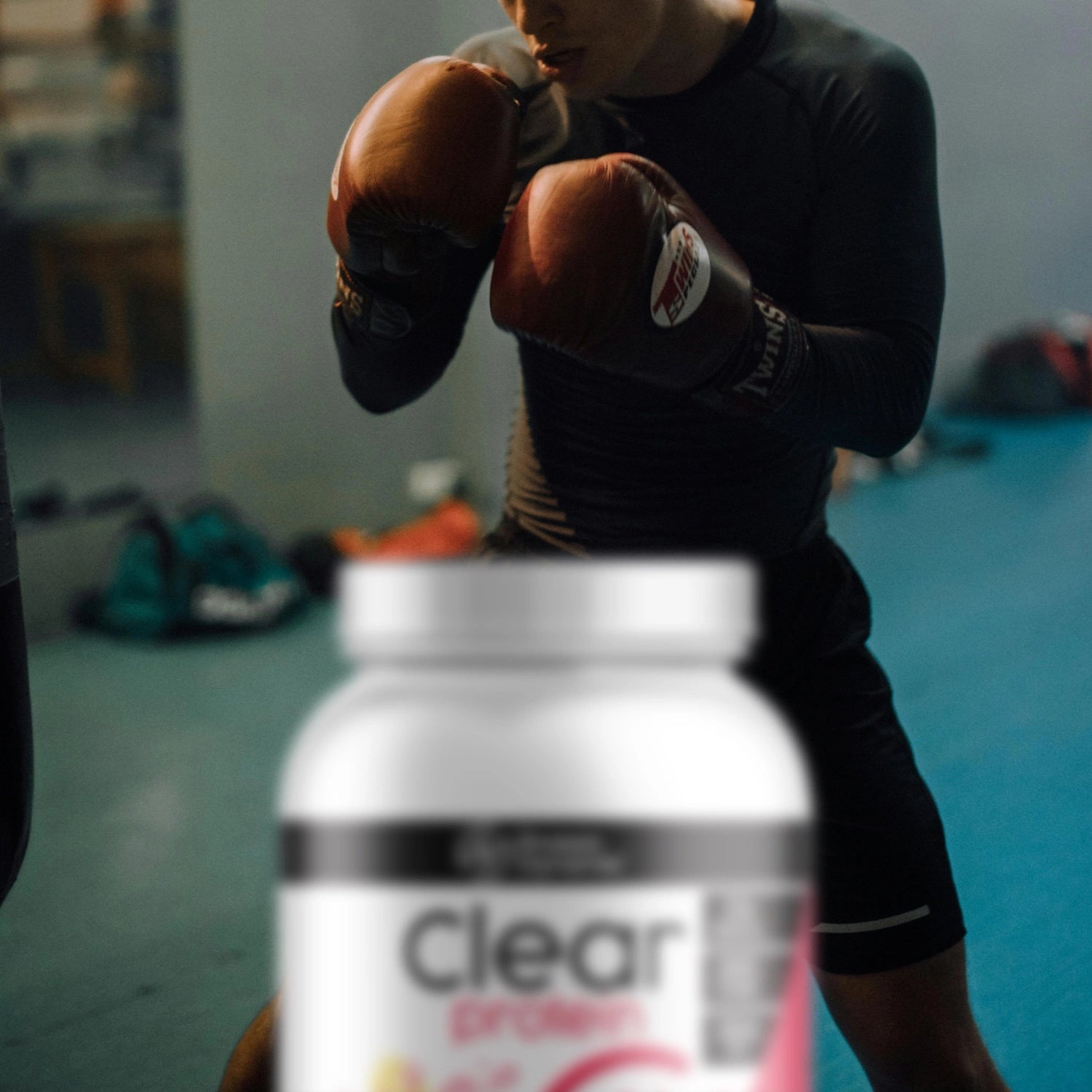 Person wearing boxing gloves with a container of Clear Protein in the foreground.
